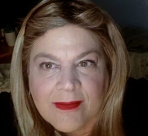 A woman with long, highlighted hair and red lipstick gazes directly at the camera, conveying confidence and warmth. Background is softly blurred.