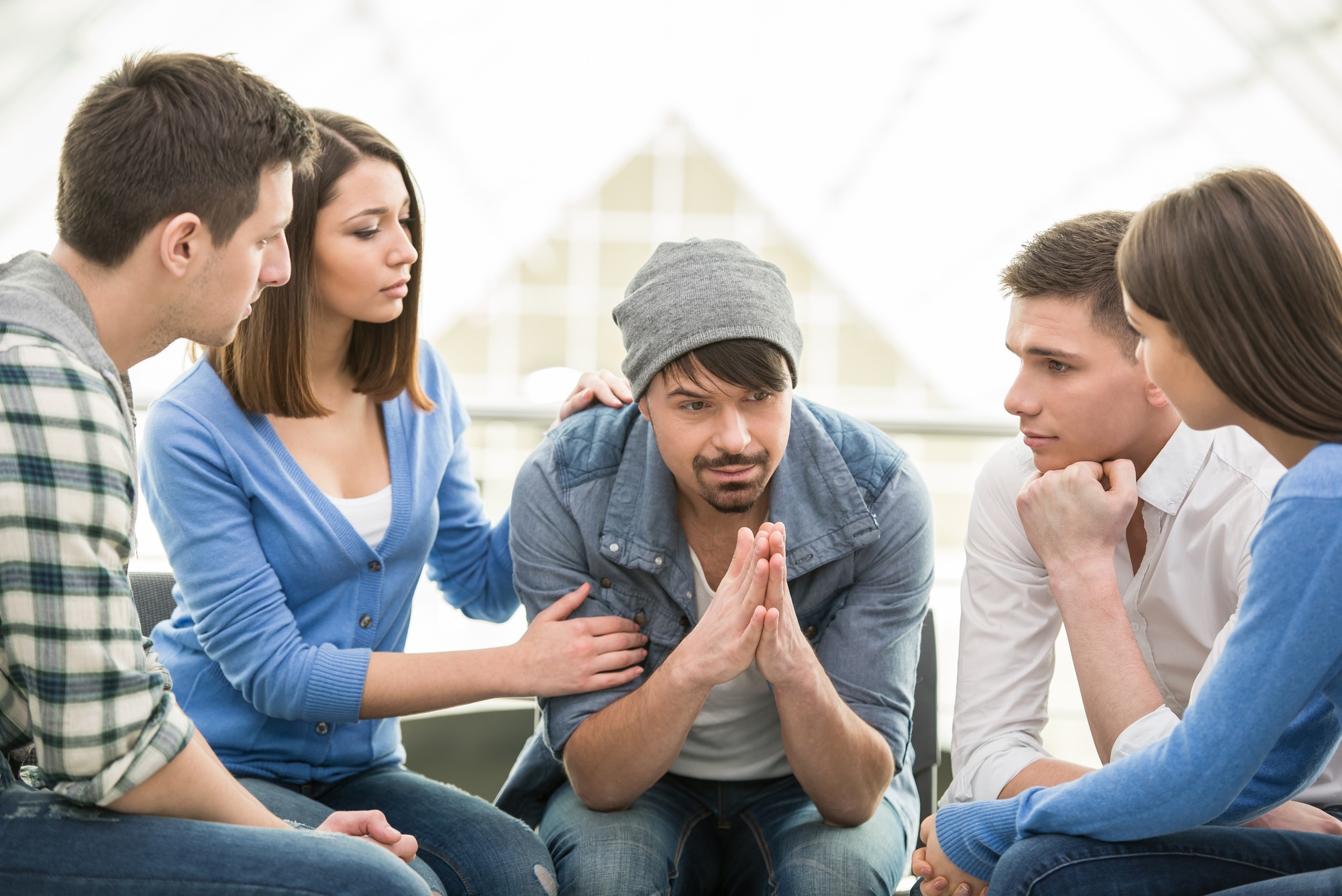 A group of five young adults engages in a serious discussion, with one individual showing signs of distress. The supportive atmosphere emphasizes communication and empathy.